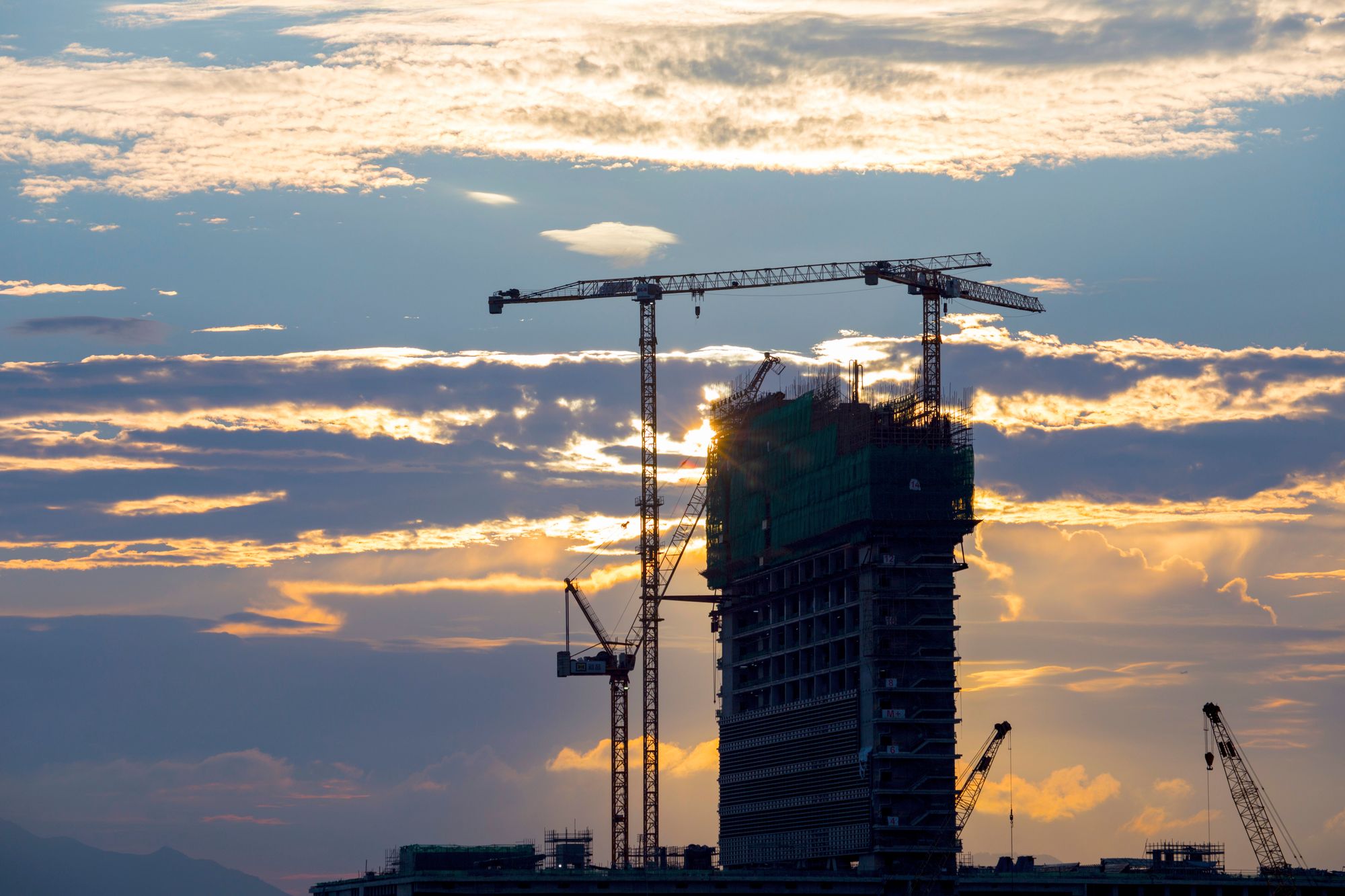 High-rise building under construction with tower cranes at sunset in Dubai